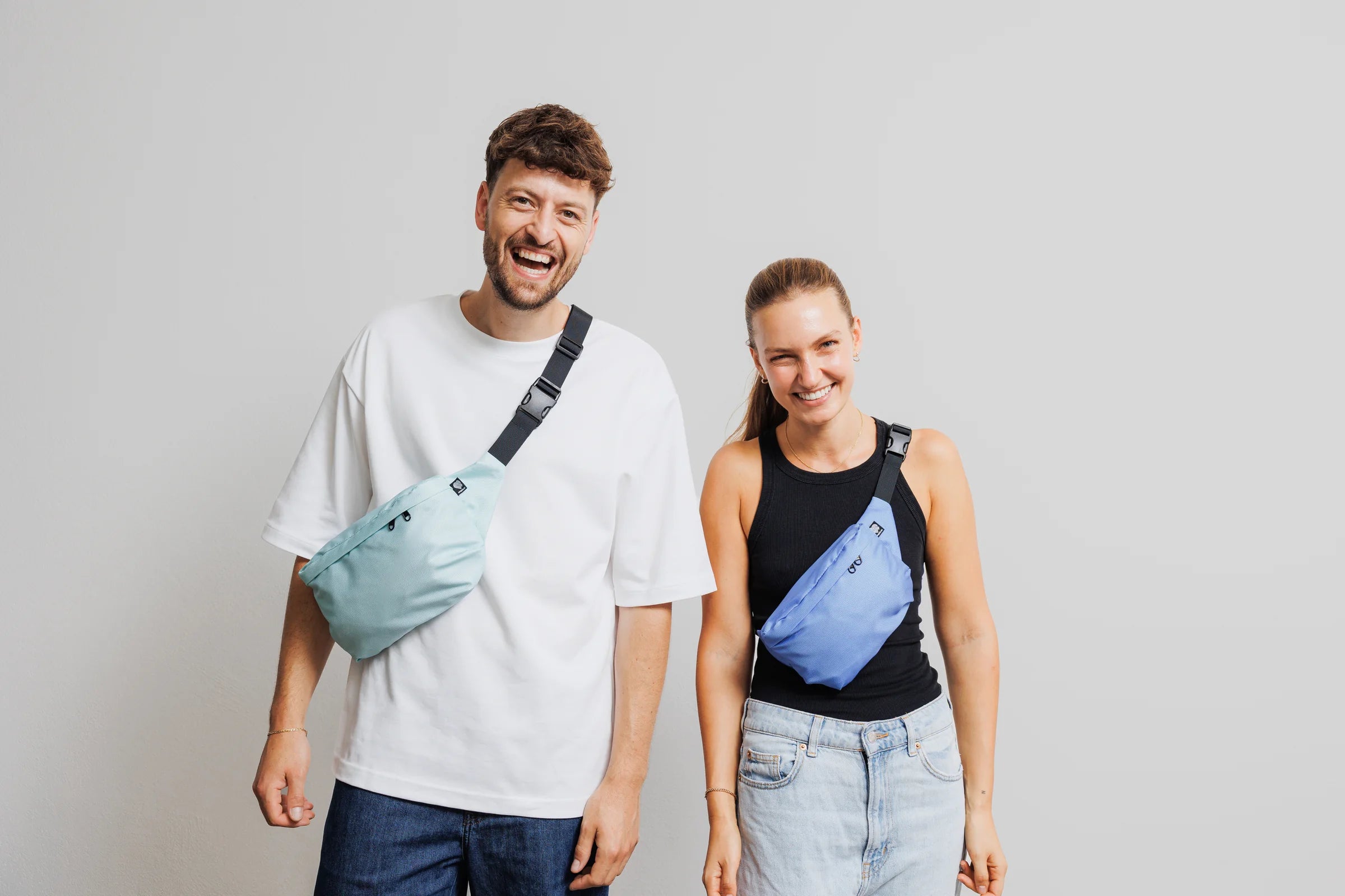 Zwei Personen tragen Bauchtaschen aus Meeresplastik in Mint und Hellblau