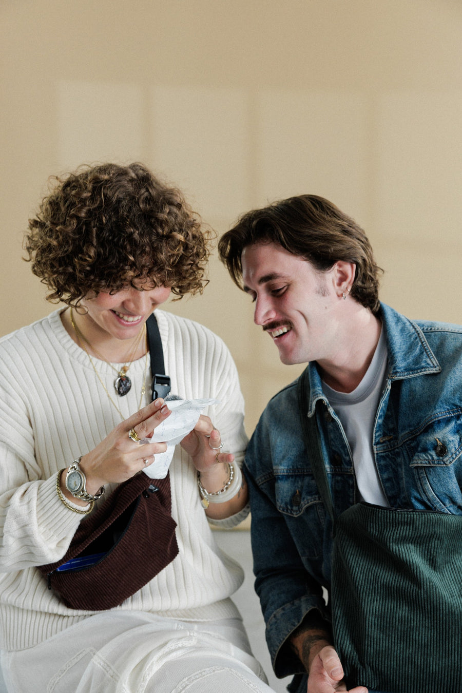 Isa und Ben lachen, Isa mit dunkelbrauner Cord-Bauchtasche, Ben mit grüner Cord-Schultertasche