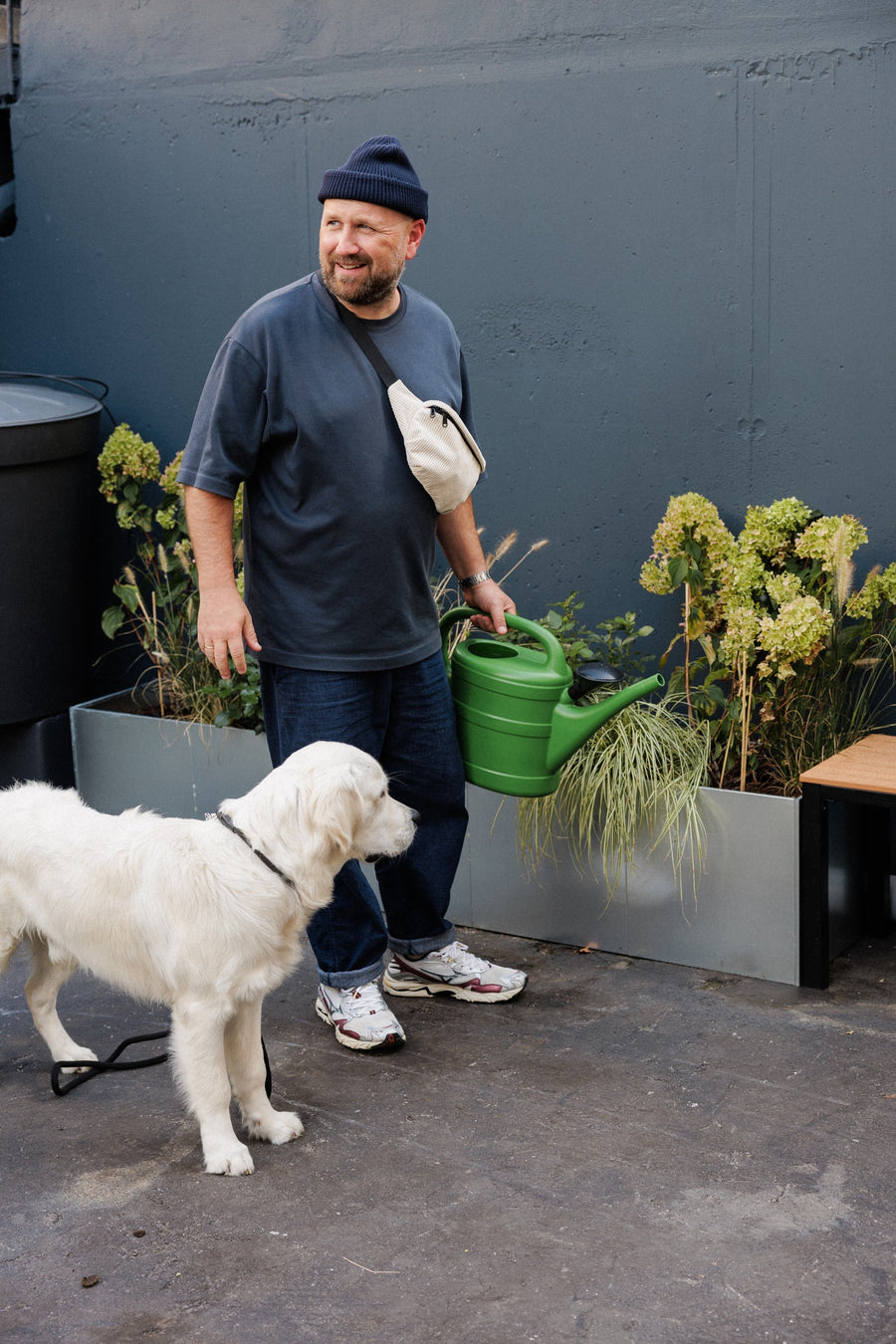 Marc mit beiger Cord-Bauchtasche und seinem Golden Retriever Charlie draußen vor einer dunklen Wand